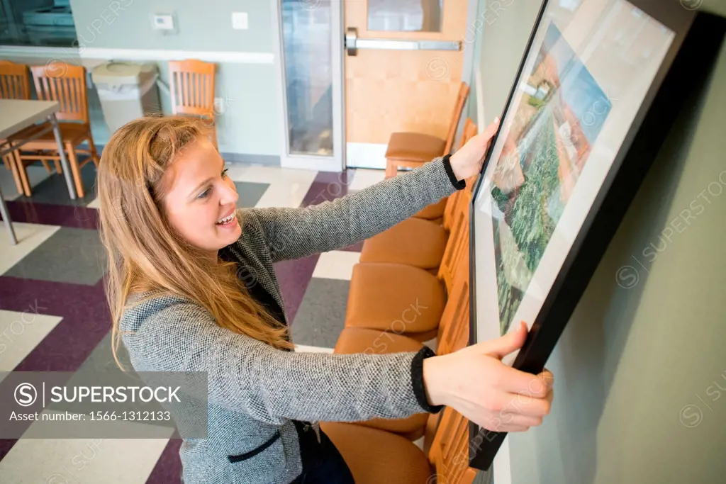 Young woman hanging photographs on wall.