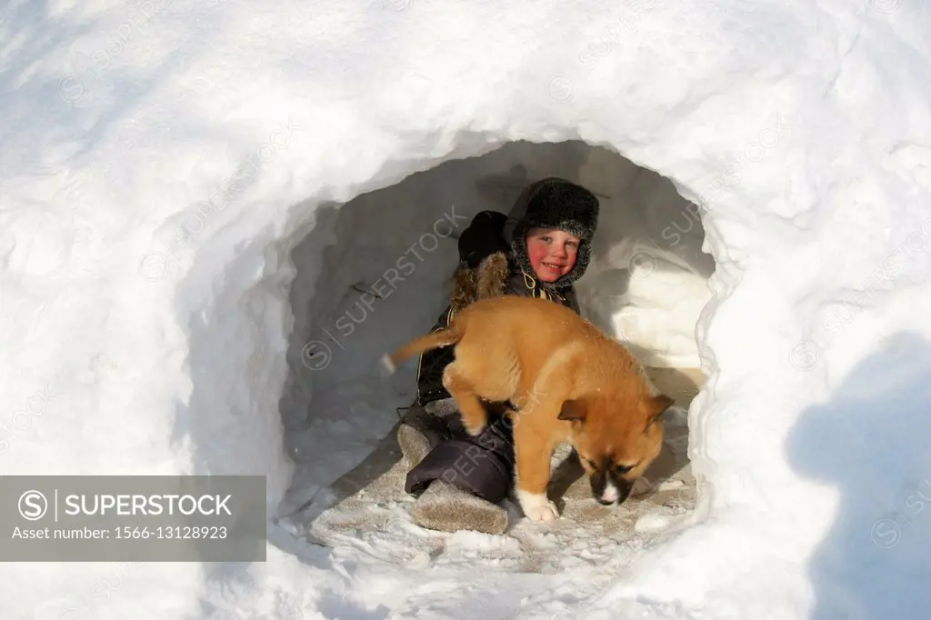 Siberia. Snowy winter. A child with a puppy playing in the snow drifts.