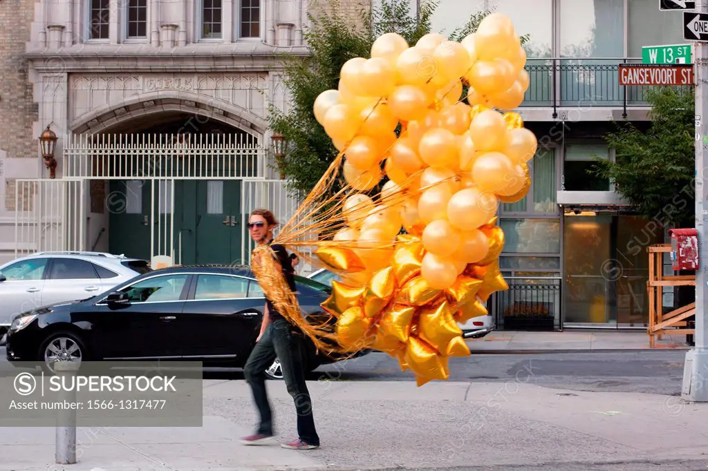 Stylish young man hurries down a Meatpacking District street with countless golden balloons in tow.