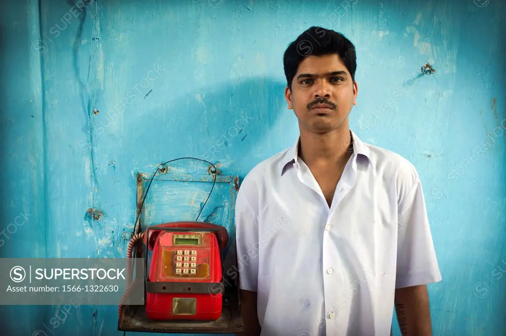 Portrait of an Indian race man leaning against a turquoise wall with red phone den stop Goa, India, Asia