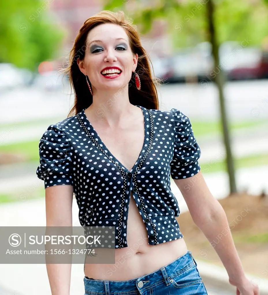 Portrait of a happy 31 year old red headed woman in an urban setting wearing jeans and a mid drift top.
