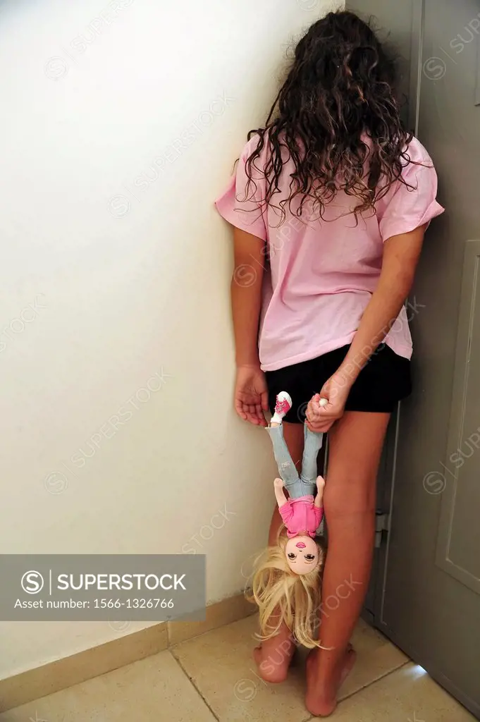 A young girl who is a victim of domestic violence stands in a corner beside the open front house door.