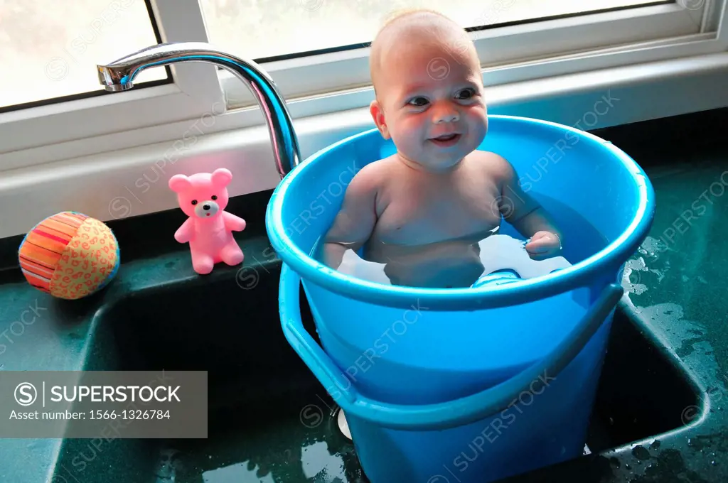 A baby in a blue bucket cools off in the summer heat.