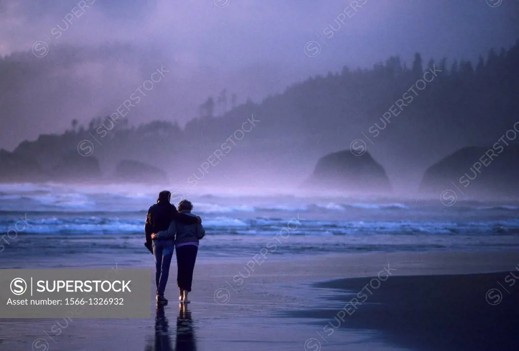 USA, OREGON, CANNON BEACH, COUPLE WALKING ALONG BEACH IN EVENING LIGHT.