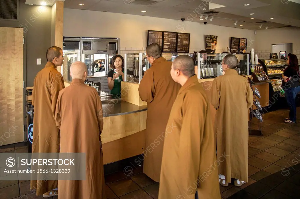 Contrasting with their workaday surroundings, three Buddhist monks and one nun in brown robes and shaved heads, purchase refreshment at Starbucks coff...