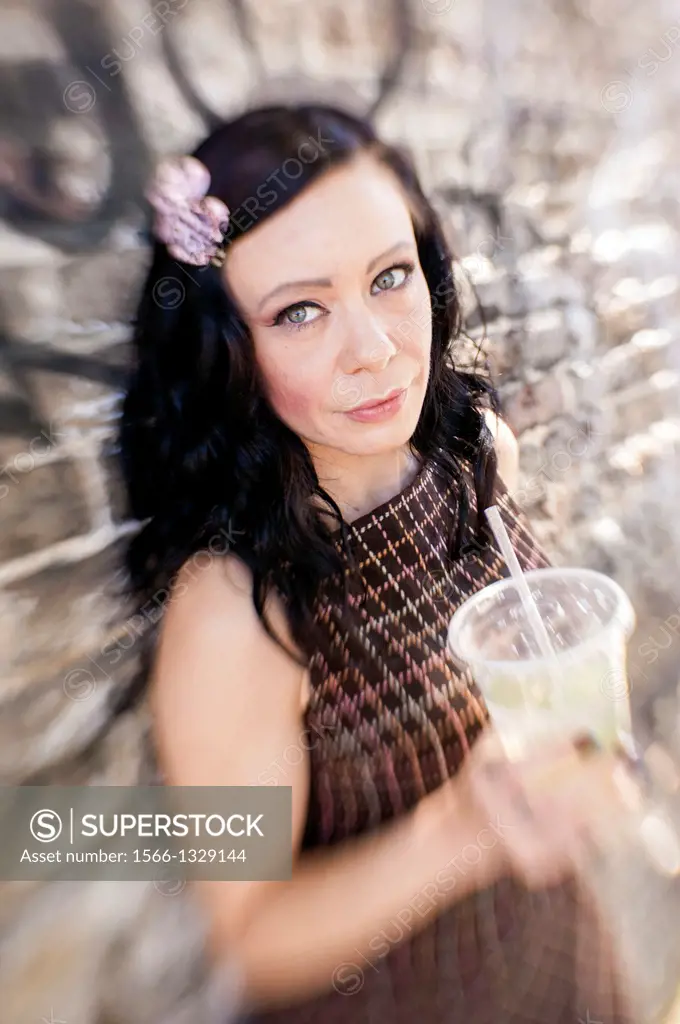 A 35 year old brunette woman holding a soft drink cup and looking at the camera.
