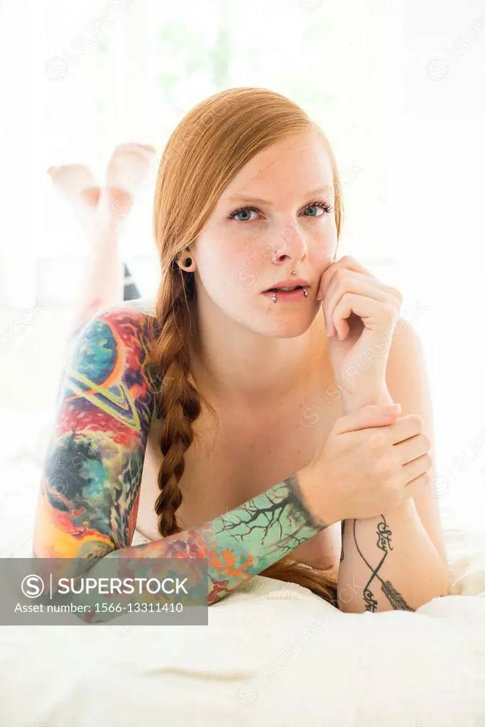 Tilburg, Netherlands. Partially nude red haired woman with sleeve tattoo lying on her bed.