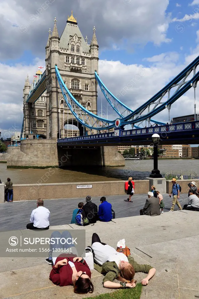 Two young women taking sunbathing on bank of River Thames with Tower Bridge in the background. London. England. United Kingdom.