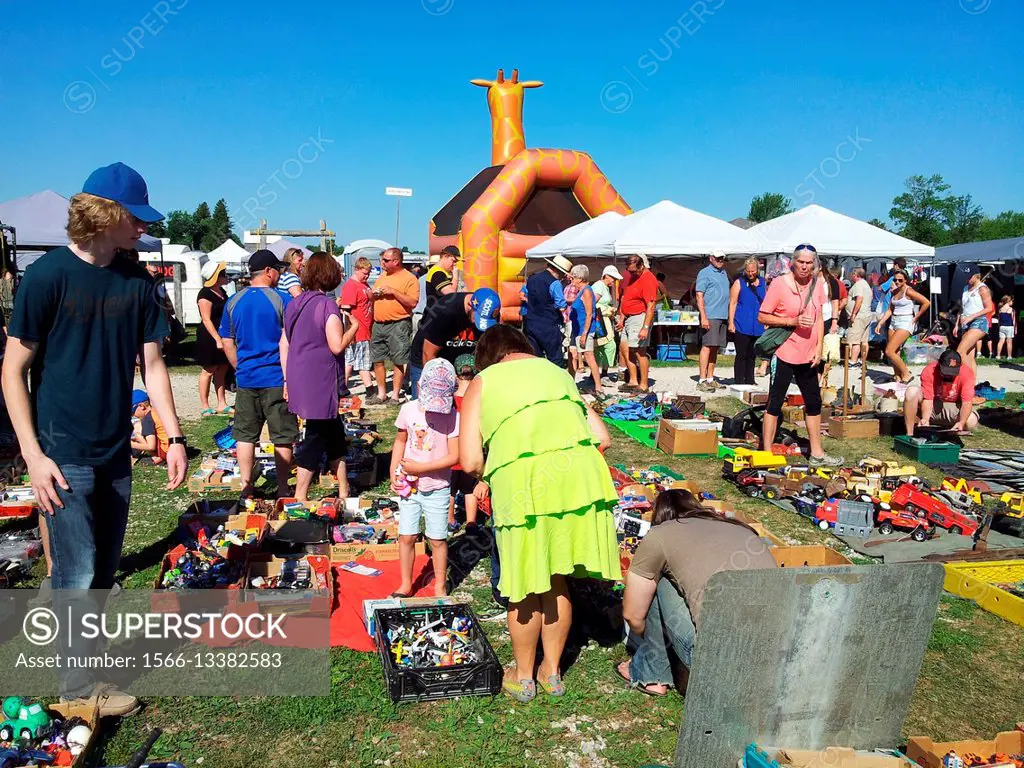 A woman in a lime green dress looks at toys on the ground at a very crowded weekly flea market including a giraffe bouncy castle in rural Ontario, Can...