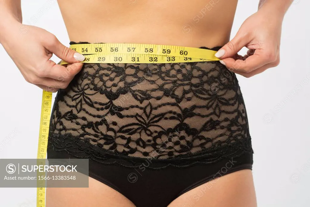 Close up of a woman in underwear measuring her waist with a tape measure.