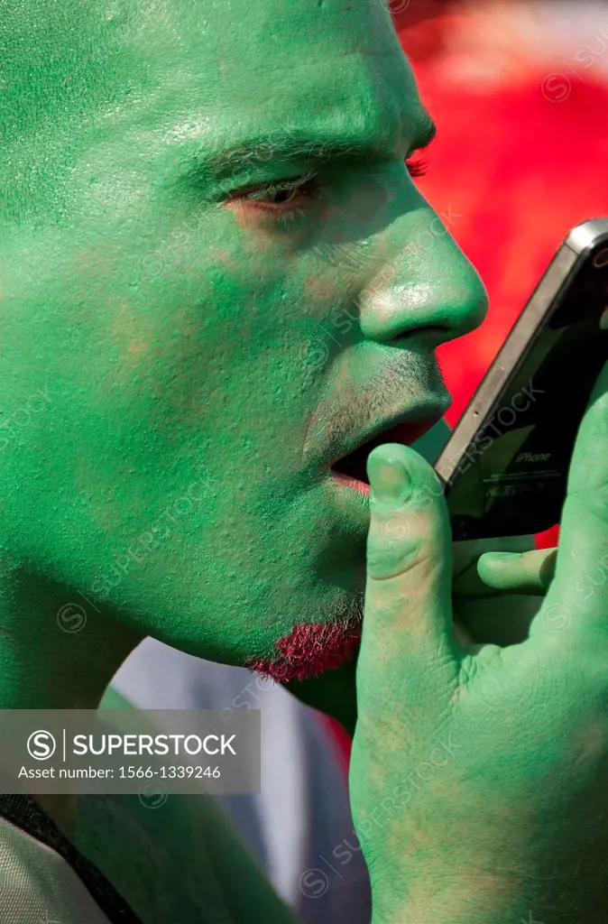 contemporary lifestyle, man´s face painted in green colour, man talking by mobile phone, taken during Lake Parade - LGBT Parade, Pride Parade, Geneva,...