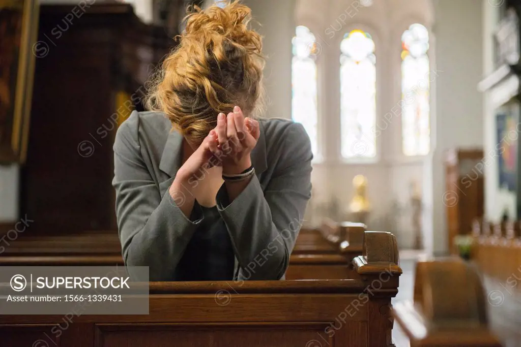 Tilburg, Netherlands. Young woman, praying to the eternal spirit, in the benches of a Roman Catholic Church.