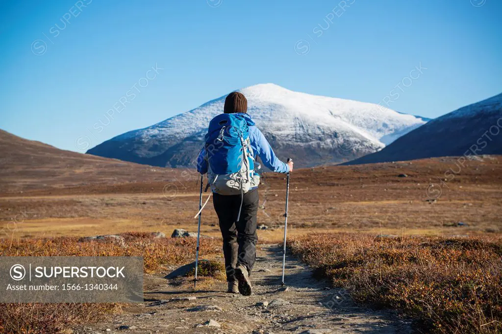Female hiker hiking north on Kungsleden trail with snow covered Keron + Giron (1543m) mountain peak in distance, Lappland, Sweden.