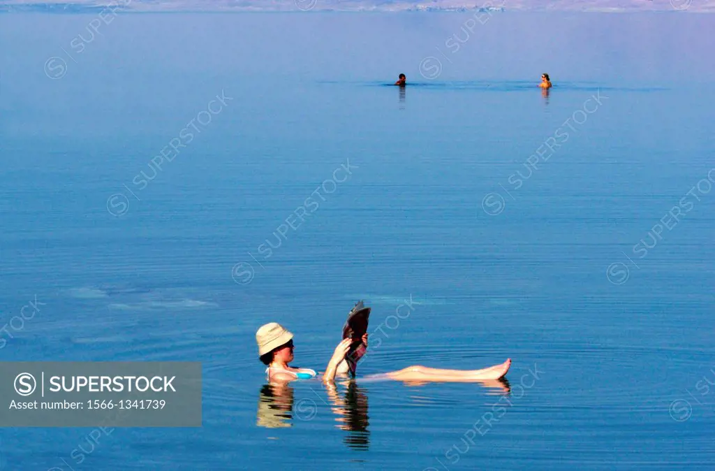 A young woman floating while reading a magazine at the Dead Sea, Israel.