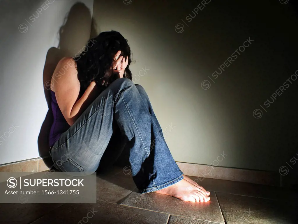 Depressed young woman sitting on the floor at home suffering from a severe depression.
