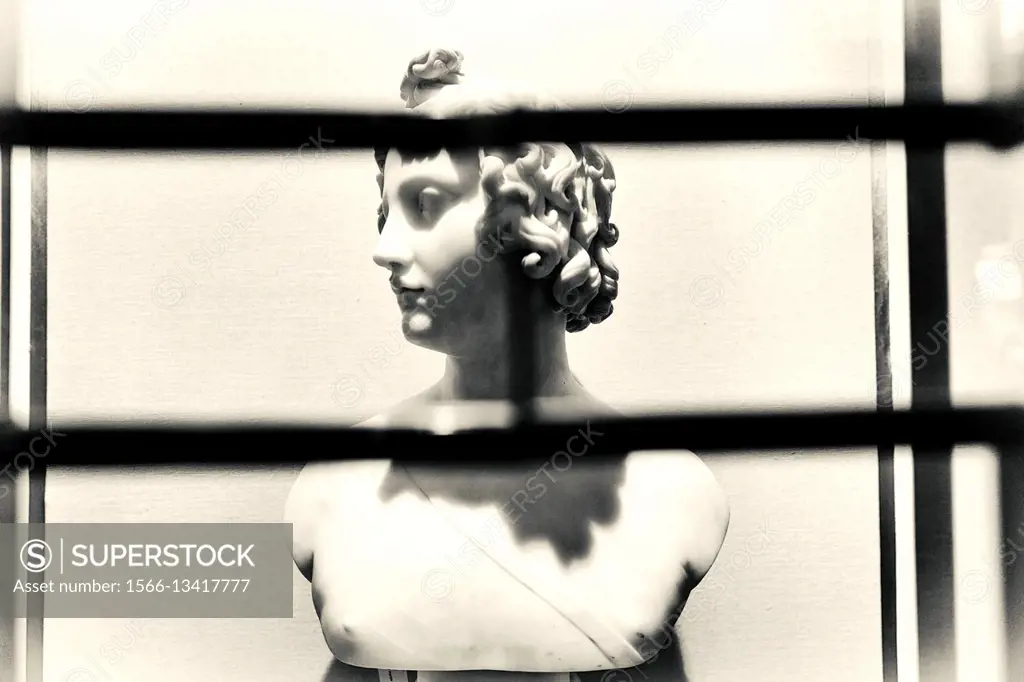 Nude female marble bust through iron gate. London, England