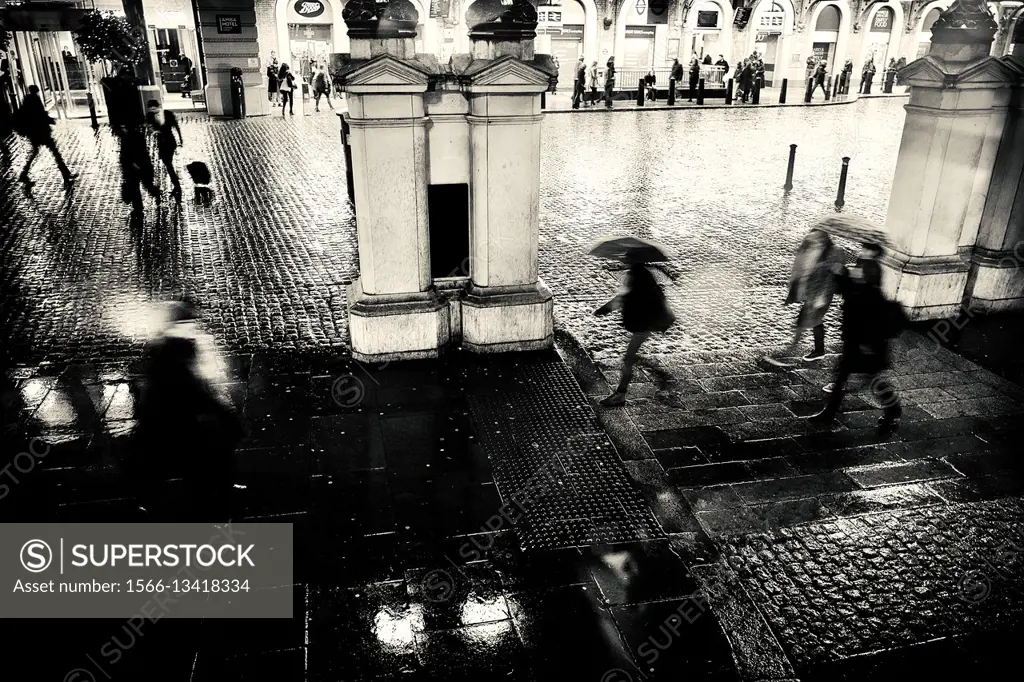 Entrance of a train station at night, rain, pedestrians with umbrellas. Charing Cross, London, England