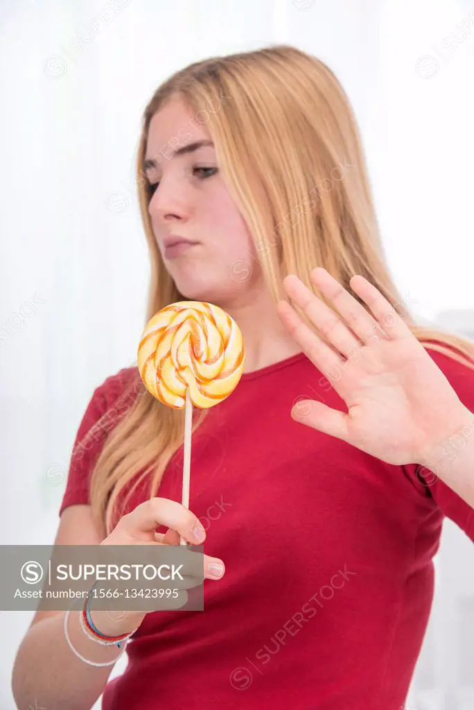 young school girl, 15 year old, in red, holding a colorful lollipop, and refusing with the other hand to eat it