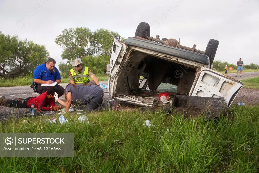 Falfurrias, Texas - A deputy sheriff and a state trooper look on while a passing motorist treats an injured man after a van holding 26 undocumented im...