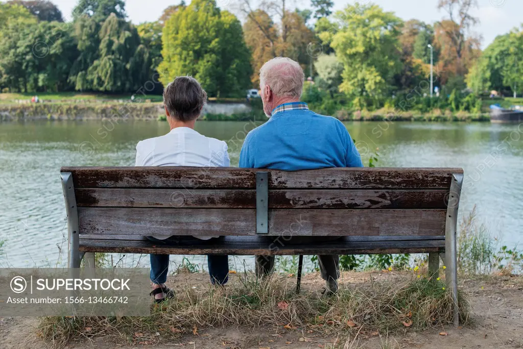 Maastricht, Netherlands. Senior adult couple enjoying their afternoon sitting on a bench and overlooking the River Maas.
