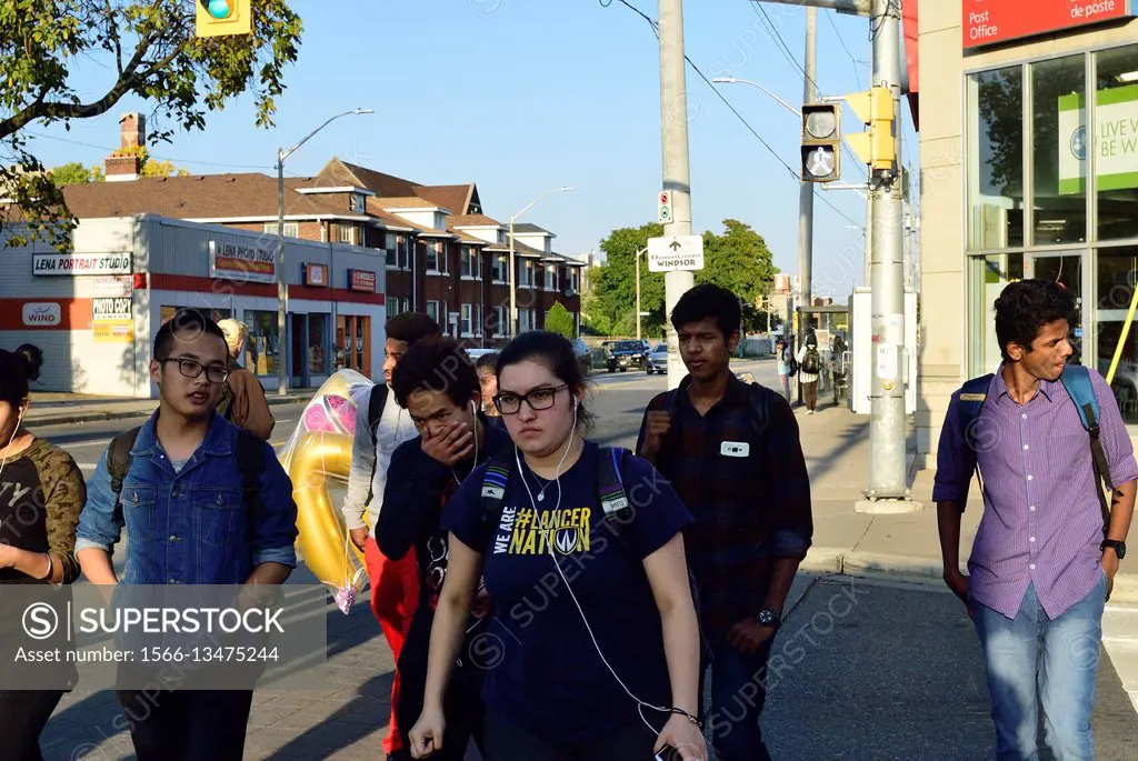 A group, mostly students, crosses an intersection in the University of Windsor area.  
