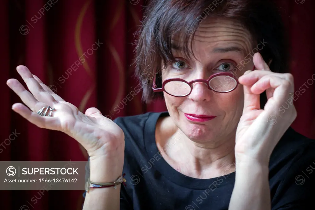 Middle-aged woman with round glasses, with one hand on the glasses and the other in accordance expression