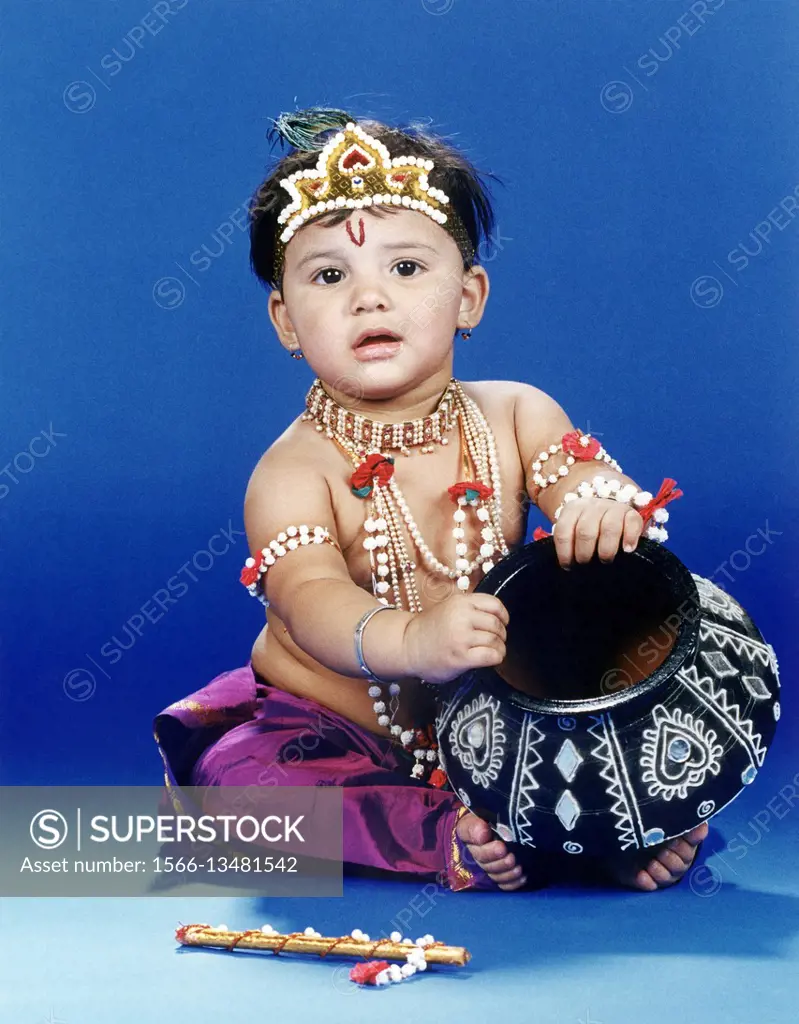 A little boy dressed as the baby lord Krishna with an earthen pot and flute.