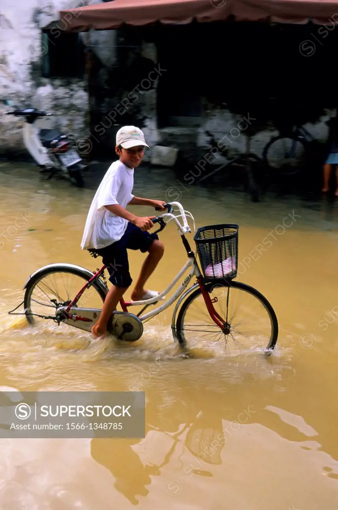 VIETNAM, HOI AN, STREET SCENE, FLOODED STREETS AFTER HEAVY RAIN, BOY ON BICYCLE.