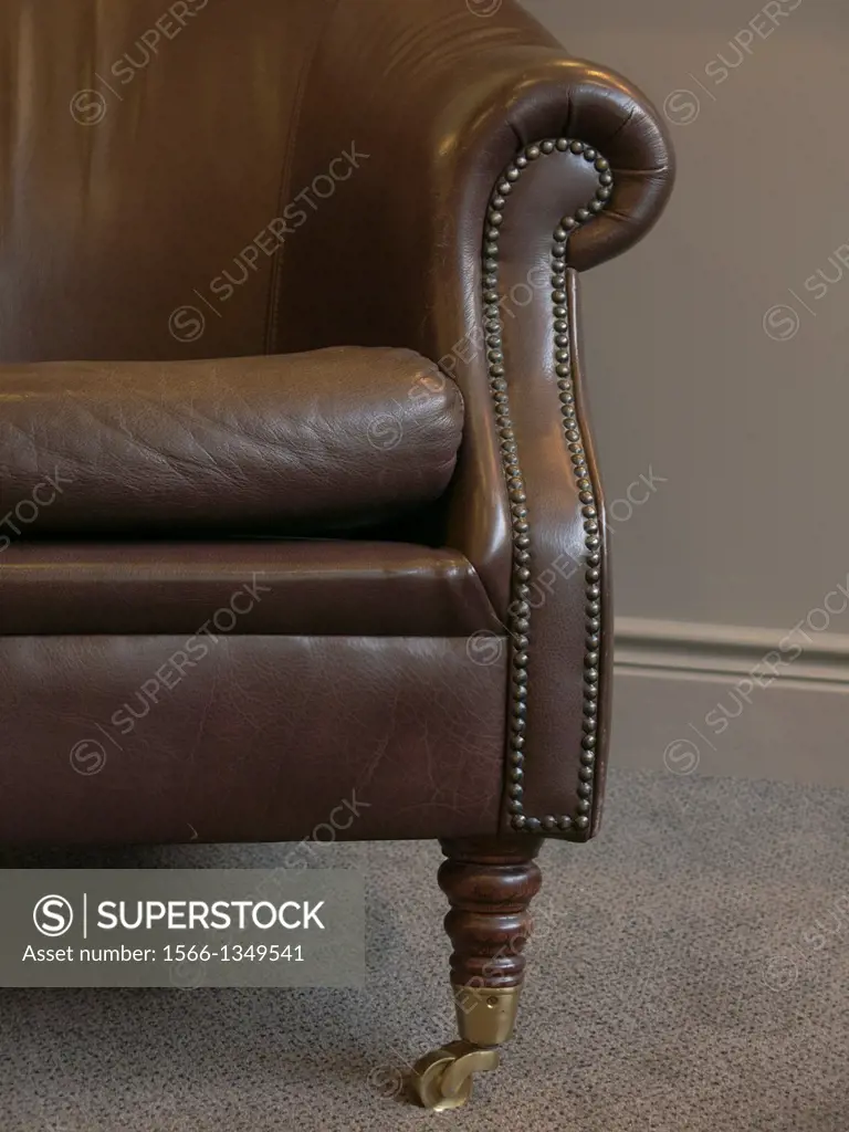 The armrest of an old leather chair with brass studs