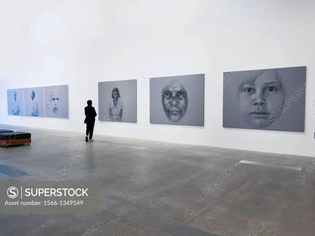 A visitor at an art gallery examines a display of large portraits . Australia