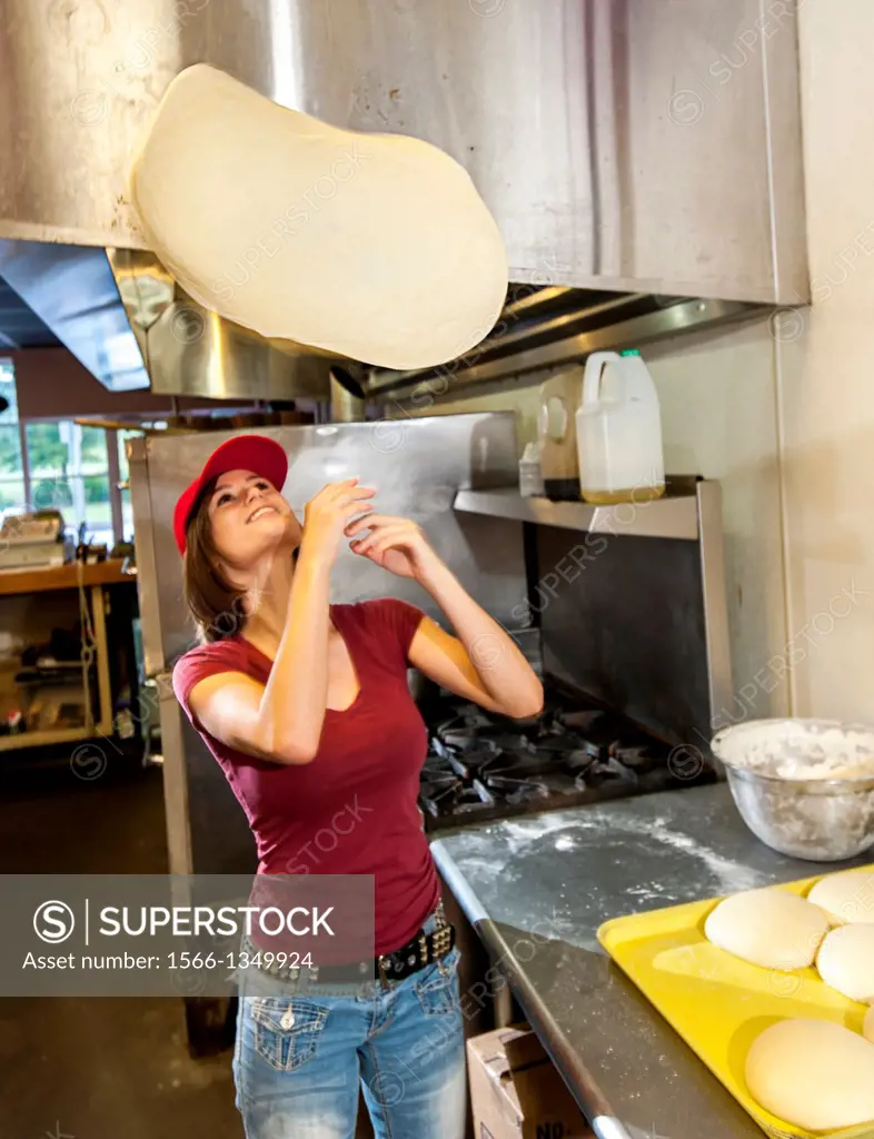 An 18 year old girl tosses pizza dough in a restaurant.