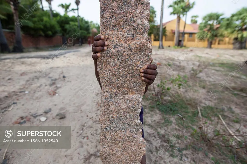 The hands of a young child hiding behind a marble fence post, India.