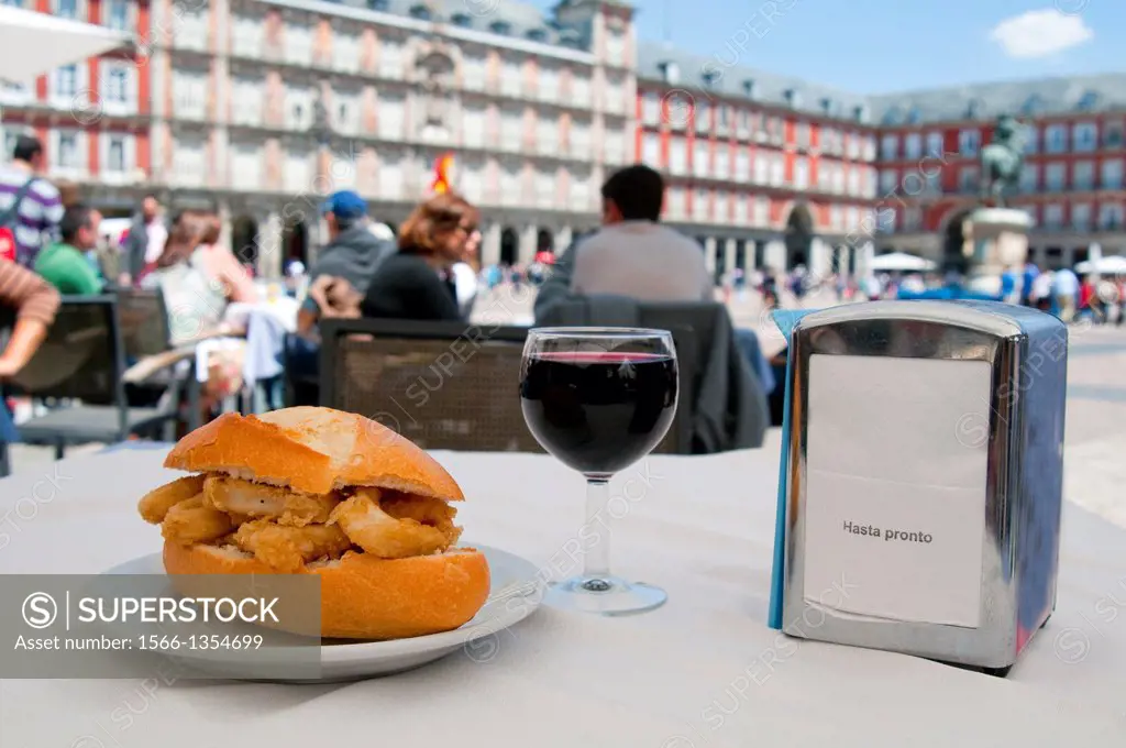 Fried squids sandwich with glass of red wine on a terrace. Main Square, Madrid, Spain.