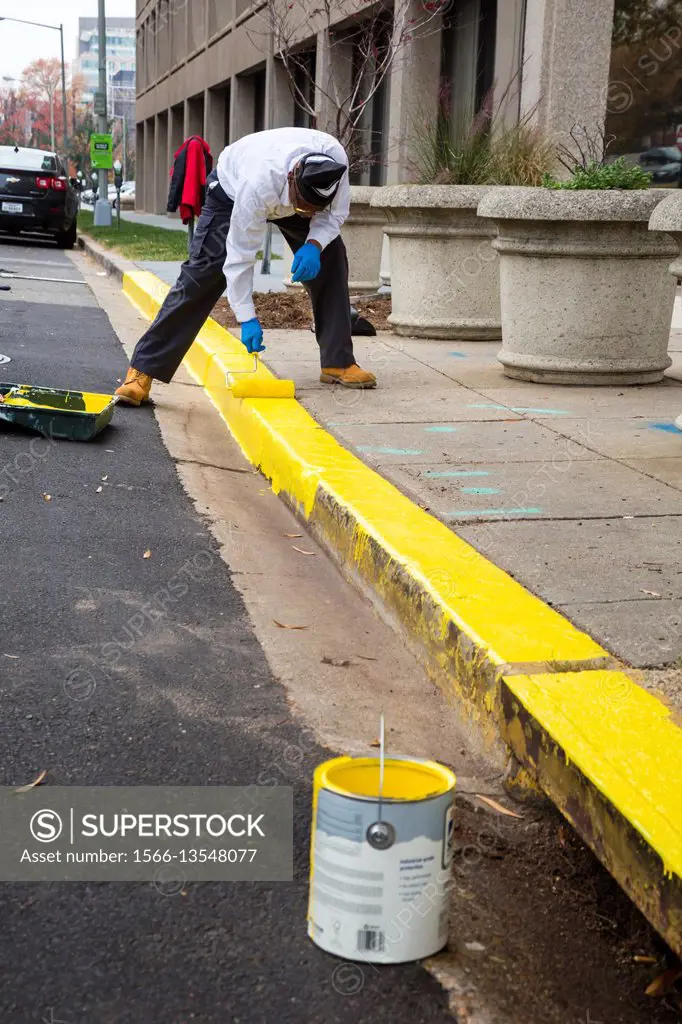 Washington, DC - A worker paints the no-parking area of the curb yellow on a city street.