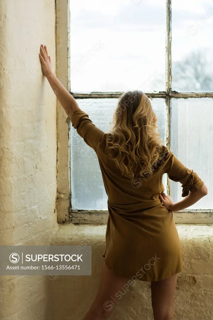 Rear view of a blond woman standing by the window.