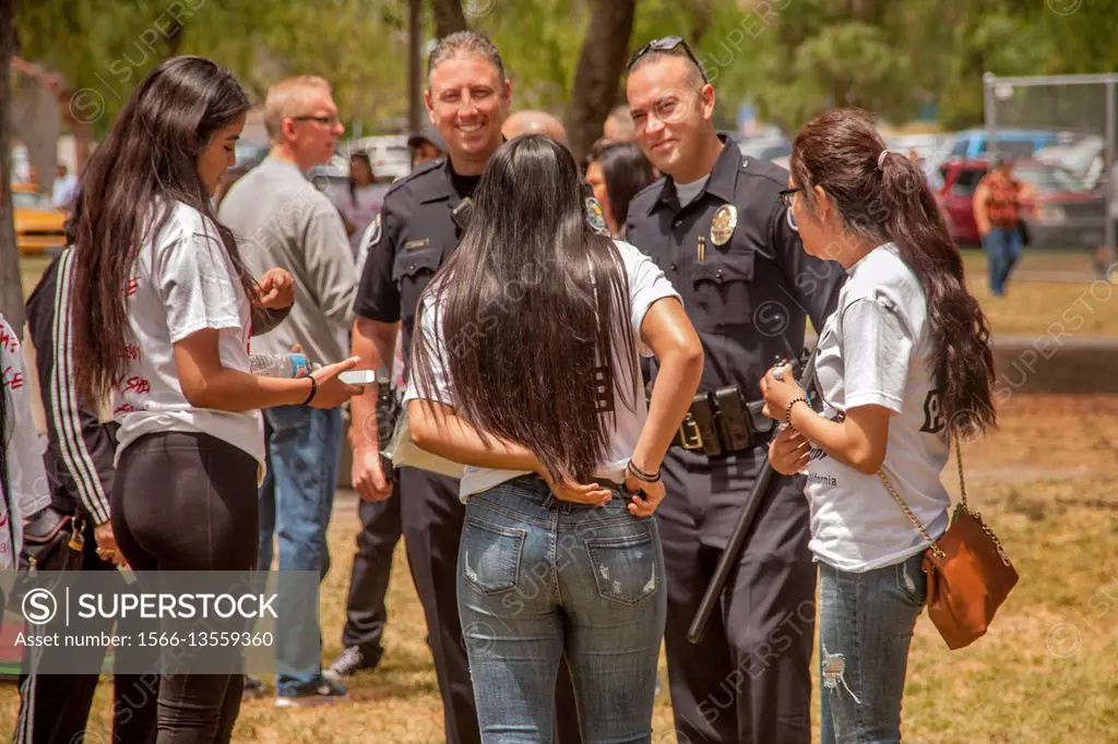 Three female young Hispanic adults chat with local police officers at an anti-violence rally in a Santa Ana, CA, city park.