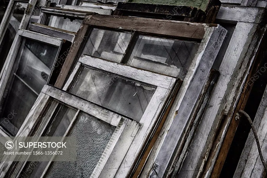 Old, weathered, antique window frames stacked together outdoors at an antique store.