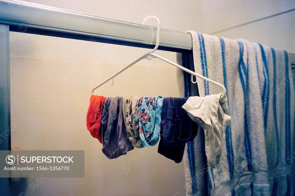 A hanger with dangling women´s underwear in a bathroom next to a towel.