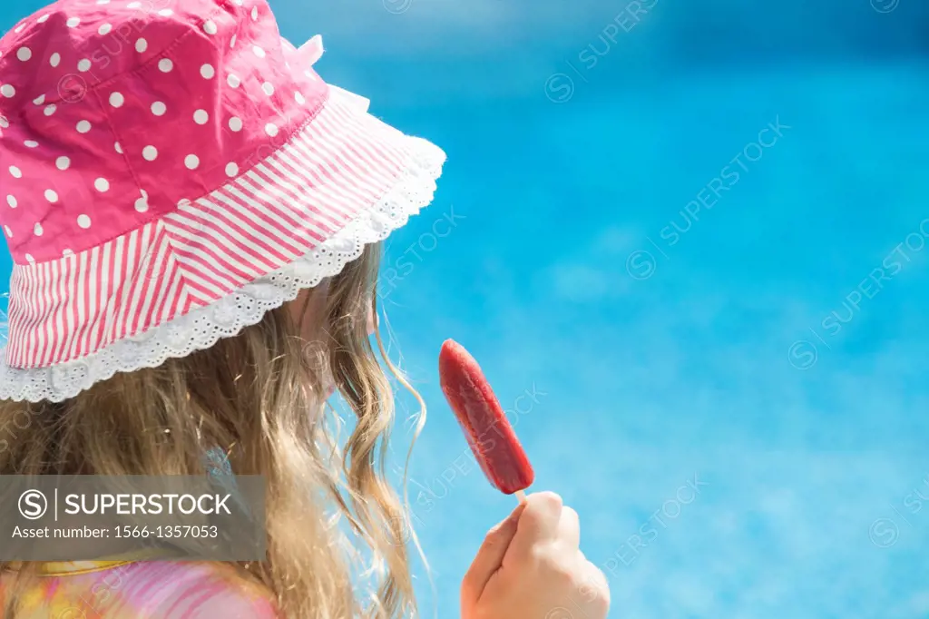 Back view of girl wearing polka dot hat eating a popsicle.