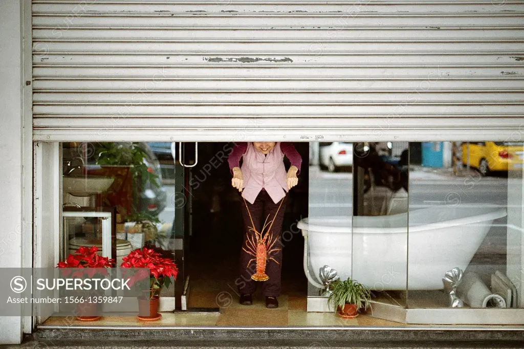 A woman holds a giant lobster by the antennae beneath a garage door in Kaohsiung, Taiwan
