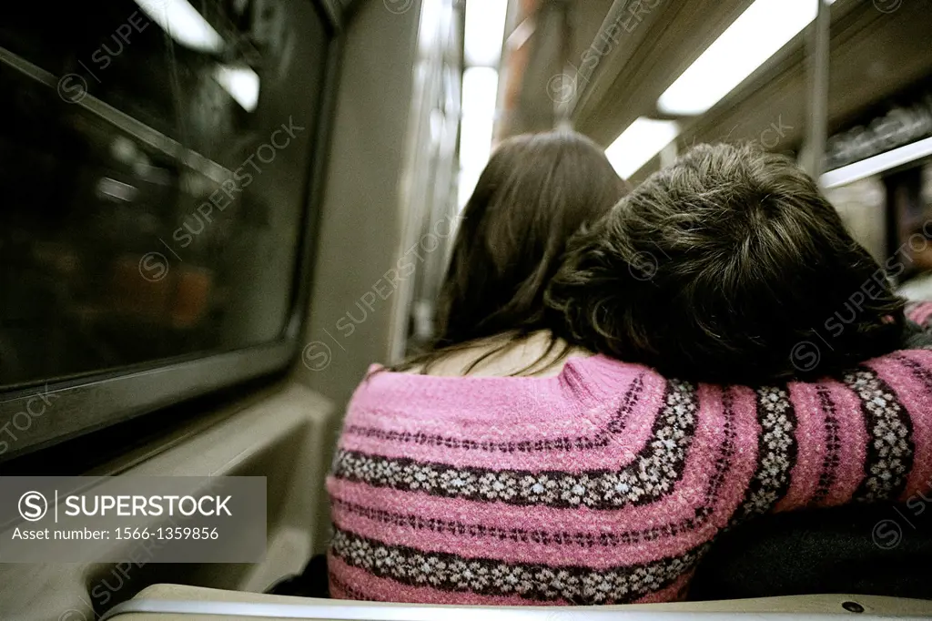 A woman in a pink sweater cradles a man´s head on her shoulder while on a subway train in New York.