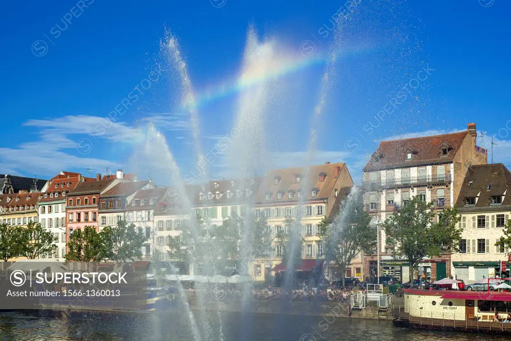 Jet of water and Quai des Pêcheurs fishermen quay with barges on Ill river and waterfront houses Strasbourg Alsace France.