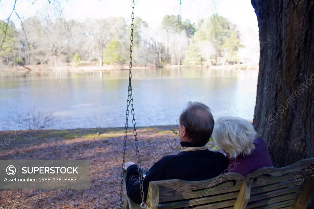 A caucasian couple in their 60´s taking a walk around a lake a sitting on a swing, enjoying retirement.