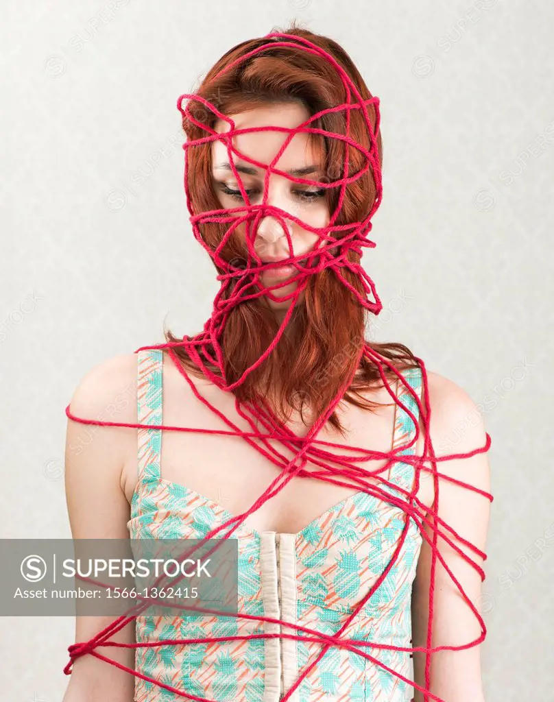 Conceptual image of woman trapped and constrained with red cotton yarn.