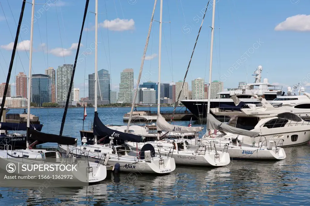 Sailboats, yachts, and pleasure boats docked in the North Cove Marina in New York City with buildings of Jersey City, New Jersey visible across the Hu...