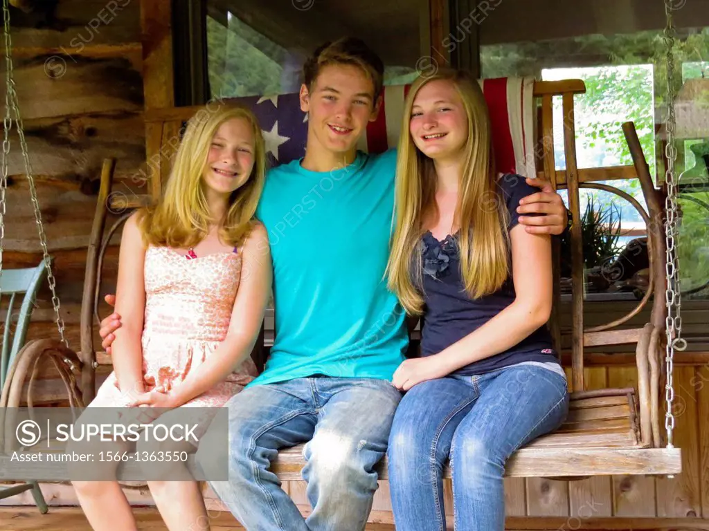 Brother hugging two sisters on porch swing