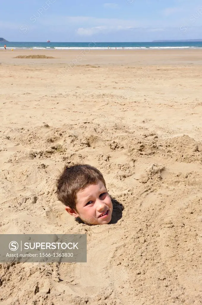 little boy buried in sand on the Kervel beach, Douarnenez, Finistere department, Brittany region, west of France, western Europe.