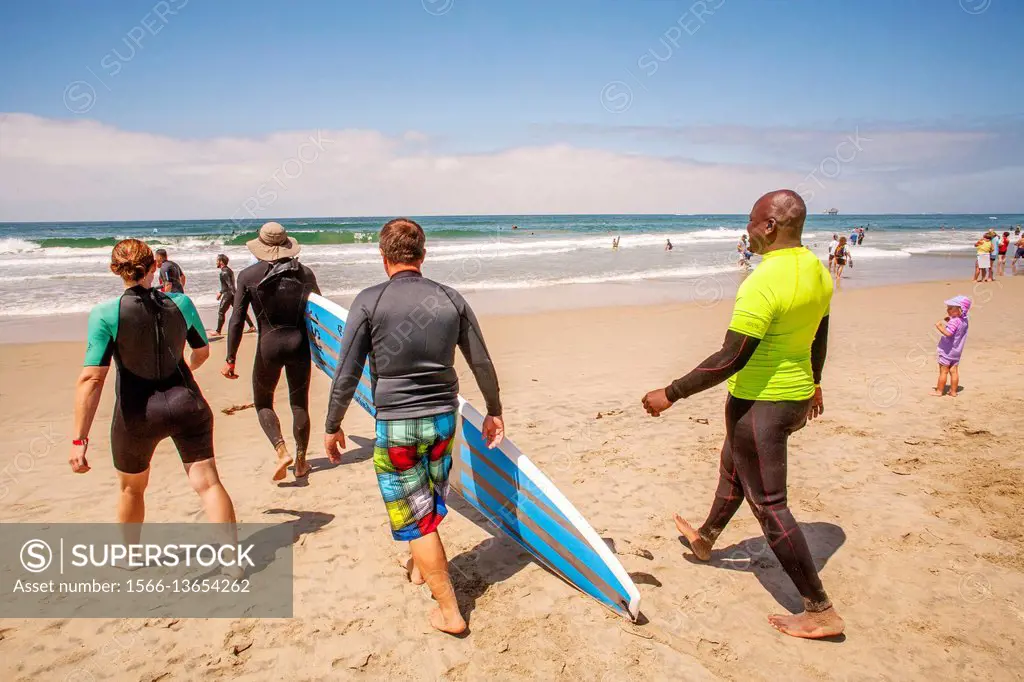 In thanks for his military service, a veteran (right) receives a free surfing lesson from a female instructor (left) as they walk to the Pacific Ocean...