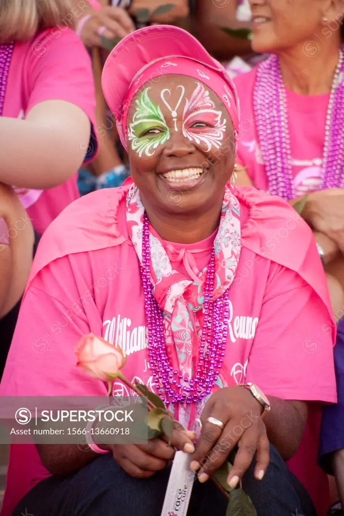 An African American breast cancer survivor is decorated with colorful face  paint at a ceremony in Newport Beach, CA. Note pink outfit and rose. -  SuperStock