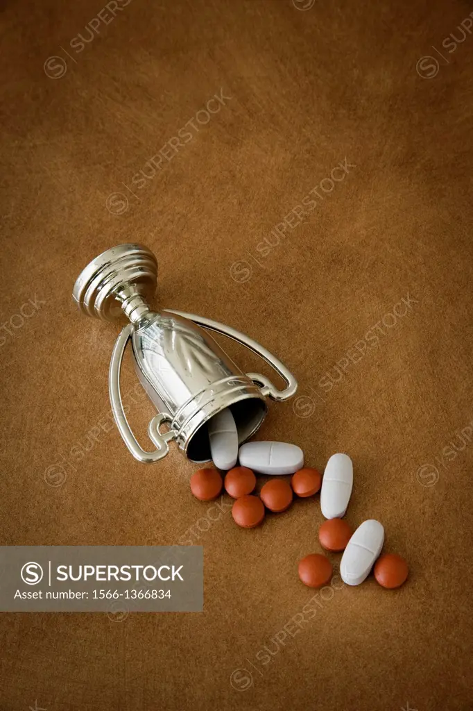 Pills falling out of an overturned trophy cup.